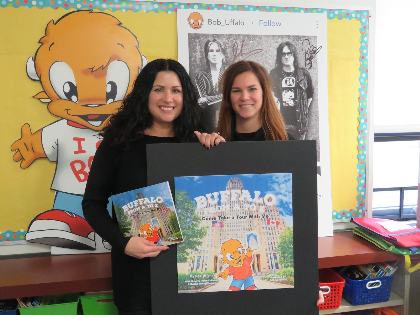 From left, Kristin Warham and Brigette Callahan show off the cover to `Buffalo From A to Z, Come Take a Tour With Me.` Also pictured behind the two authors, from left, a cardboard cutout of character Bob Uffalo and an autographed picture from Buffalo's own, the Goo Goo Dolls. (Photo by David Yarger)